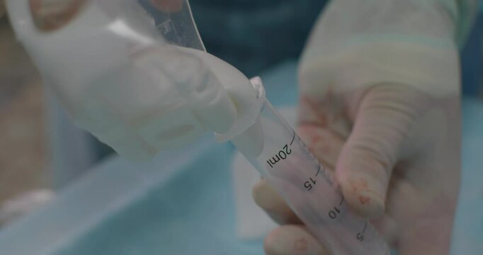 Filling a syringe with bone cement to fix a broken vertebra. Gloved hands carefully prepare bone cement in a syringe for an animal's spinal surgery, highlighting the precision of veterinary surgery.
