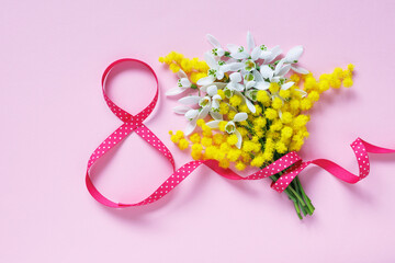 Number eight from a ribbon and a bouquet of snowdrops with mimosa on a pink background. Postcard for International Women's Day, March 8