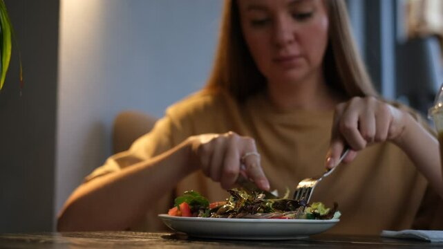 a young woman of European appearance eats a vegetable salad in a cafe