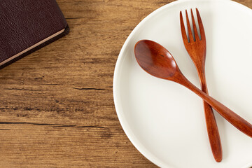 Empty plate with spoon and fork and holy bible book on wooden background. Top view. Christian fasting and spiritual food, biblical concept.
