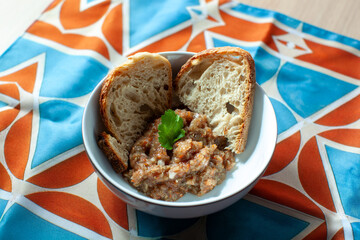Bowl of eggplant caviar, also known as aubergine caviar, served with two slices of bread and garnished with a coriander leaf, placed on a colorful tablecloth