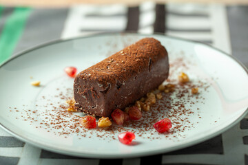 Chocolate potato cake sprinkled with cocoa powder served on white plate decorated with pomegranate seeds and walnuts