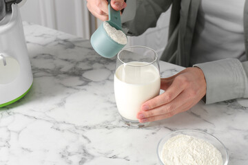 Making protein cocktail. Woman adding powder into glass with milk at white marble table, closeup