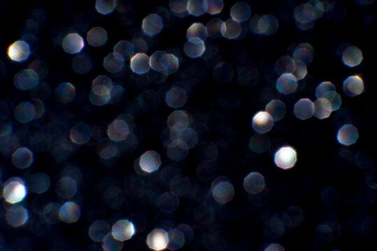 Sparkling bokeh lights on a dark background with hexagonal shapes and soft glow effects.