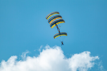 Scenic parachutists formation airshow with yellow-blue ukrainian parachutes above clouds