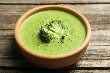 Delicious broccoli cream soup in bowl on wooden table, closeup