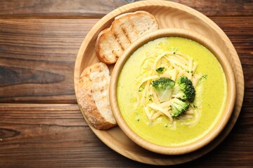 Delicious broccoli cream soup in bowl and croutons on wooden table, top view. Space for text