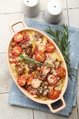 Delicious pasta casserole in baking dish, rosemary and spices on tiled table, flat lay