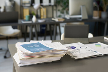 Stack of financial documents with graphic information standing next to open folder with other...