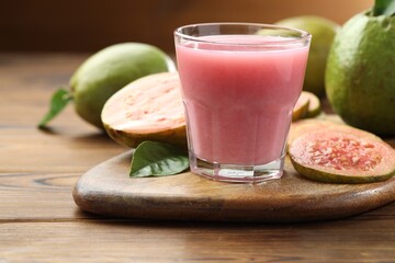 Tasty guava juice in glass, leaves and fruits on wooden table, closeup