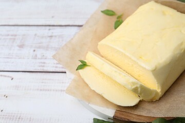 Cut brick of butter and basil on white wooden table, closeup. Space for text