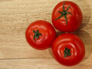 Freshly picked tomatoes resting on a wooden table, showcasing vibrant red hues and lush green stems for a rustic touch