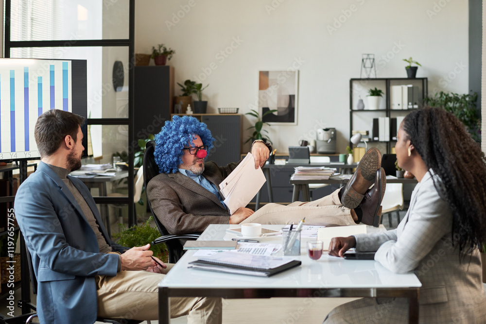 Poster clown boss keeping legs on desk and looking through financial papers while sitting in front of two y