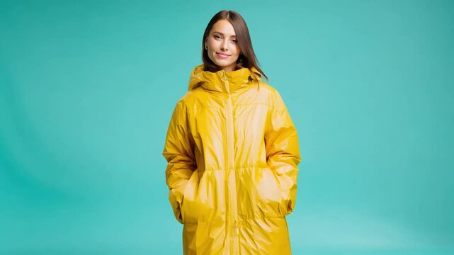Static video of model standing in vibrant teal backdrop, wearing a yellow raincoat with bright lighting emphasizing the colors
