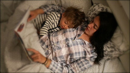Mom reading bed-time story to toddler son at night before sleep