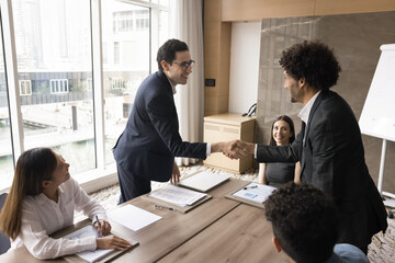 Young Arabian male business partners in suits shake hands over conference table, make agreement,...