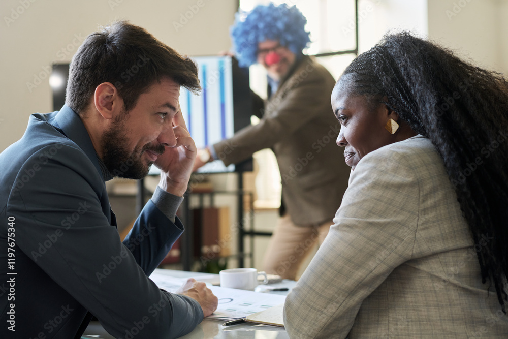 Aufkleber two young smiling subordinates looking at one another while making fun of their boss wearing clown w
