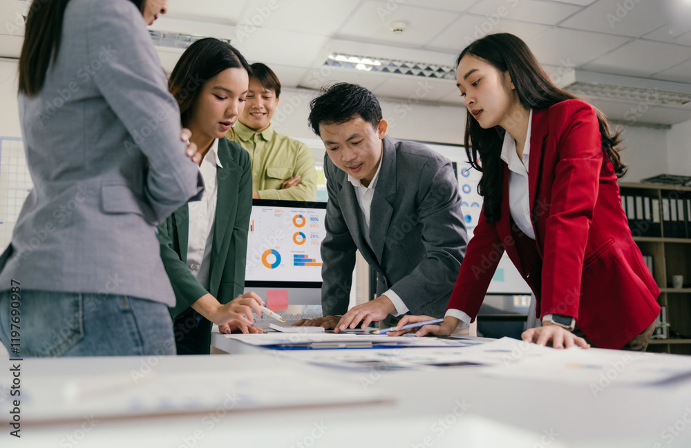 Poster Focused asian businesspeople working together, analyzing charts and reports on a table in a modern office, discussing strategies and financial data displayed on a computer screen