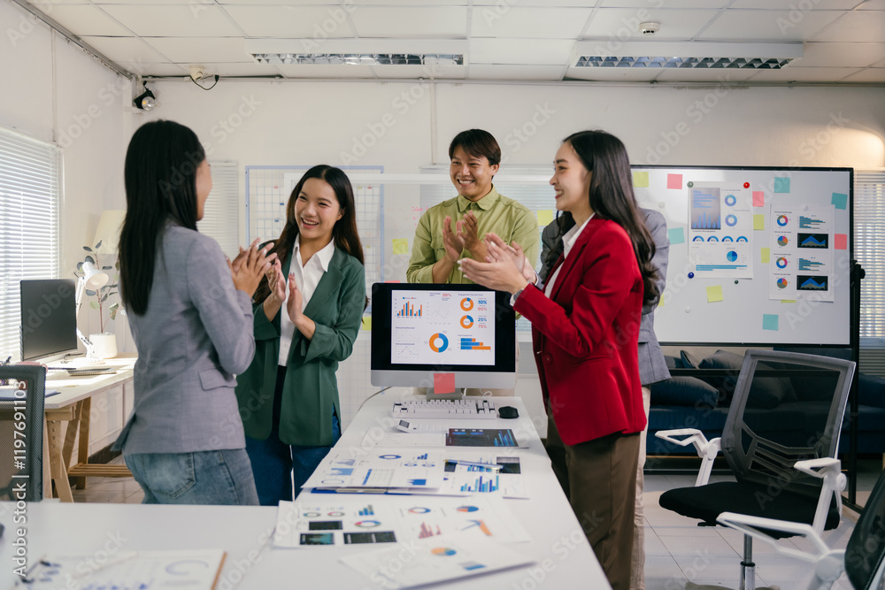 Poster Four asian marketing professionals are clapping their hands together in the office. Celebrating a successful business project. Standing in front of a computer screen showing positive data and charts