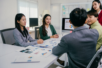 Asian businesspeople are discussing and brainstorming together during a meeting in a modern office, analyzing financial statistics displayed on a computer screen