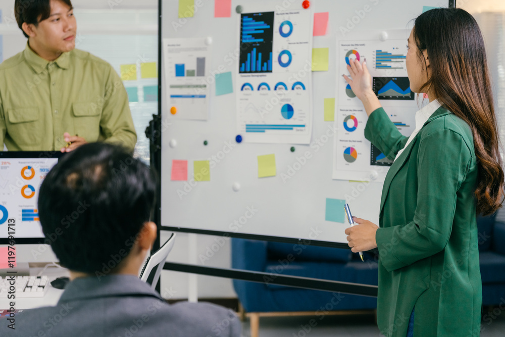 Poster businesswoman pointing at charts and explaining strategy to colleagues during a meeting in a modern 