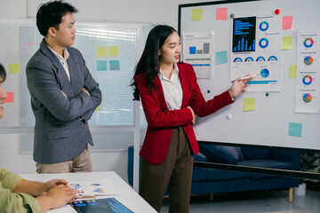 During a business meeting, a businesswoman uses a whiteboard with charts and graphs to explain statistics and data analysis to her colleagues, fostering collaboration and strategic decision-making