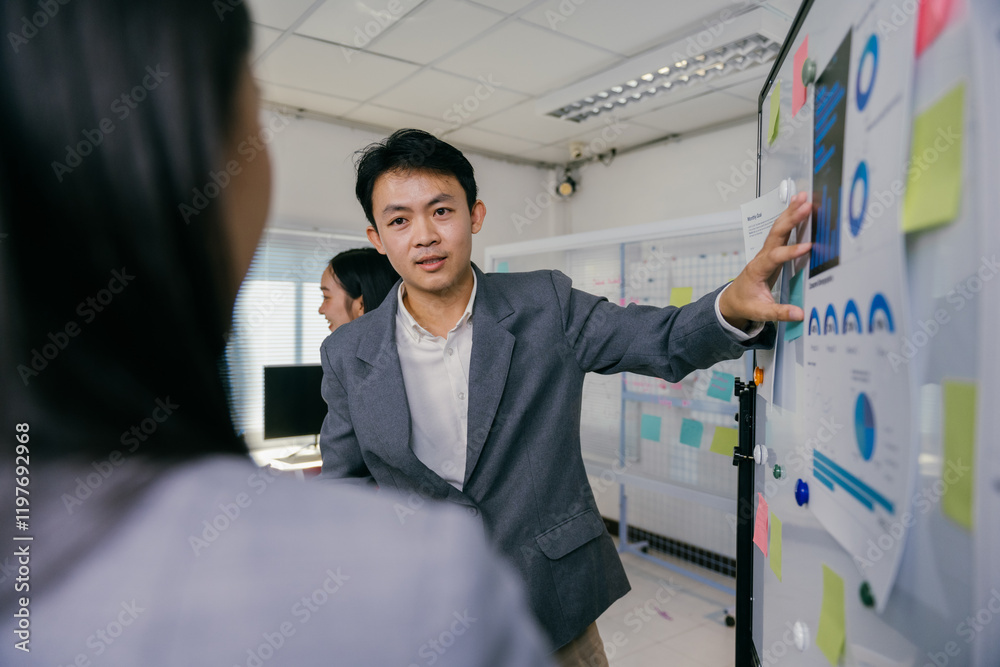 Poster asian businessman is pointing at charts and graphs on a whiteboard while giving a presentation to hi
