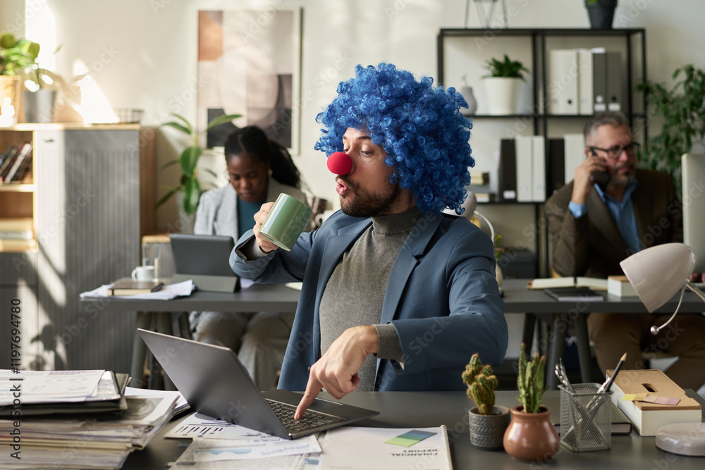 Poster Young businessman in clown wig looking at mug with coffee and pressing key of laptop keypad while having break in office
