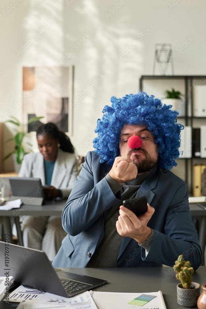 Poster angry young clown employee showing fist in smartphone screen while communicating with colleague in v