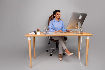 Full body photo of attractive young businesswoman sit table work computer dressed stylish formalwear isolated on gray color background