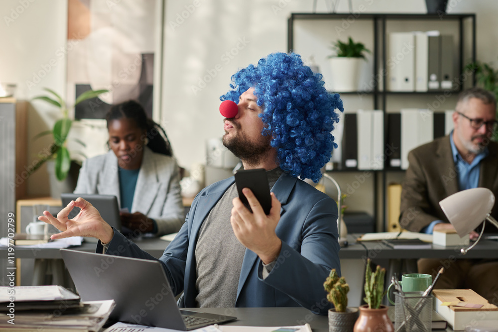 Poster young clown employee with smartphone in hand watching online yoga course and relaxing by workplace i