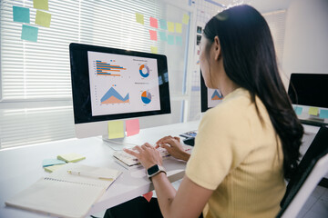 Focused businesswoman analyzes financial data in a modern office, surrounded by technology and sticky notes. She embodies success in the corporate world