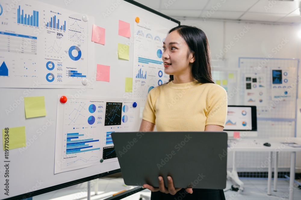 Poster young professional standing in a modern office, holding a laptop and presenting business data and in