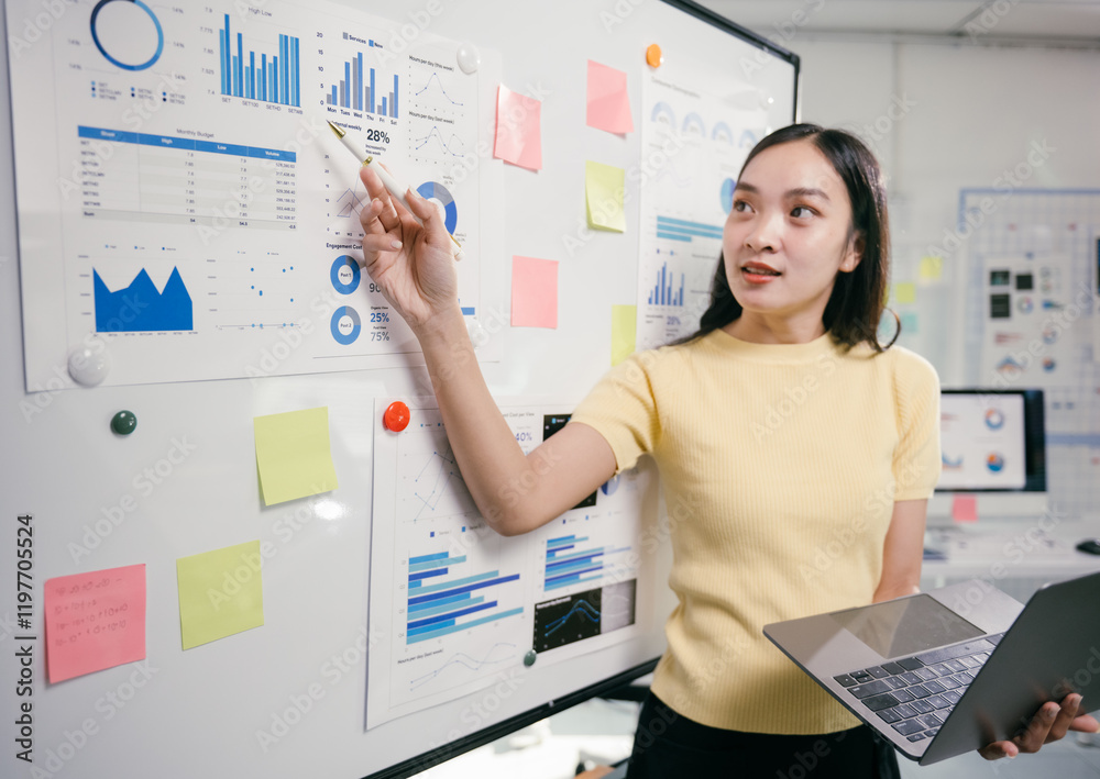 Aufkleber businesswoman is pointing at charts and graphs on a whiteboard while holding a laptop in her other h