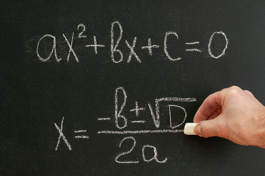 The teacher writes the formula of quadratic equation  on a blackboard with chalk
