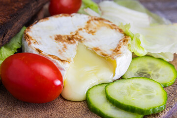 Detail of flowing grilled camembert cheese with cucumber, tomato and salad on wood plate. Vegetarian, healthy homemade food