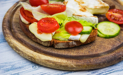 Grilled camembert cheese on bread with cucumber, tomato and salad on wood plate. Vegetarian, healthy homemade food