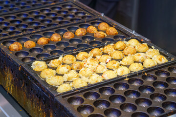Osaka, Japan - Sep 21 2024, A close-up view of takoyaki cooking in a frying pan, a national Japanese dish in the form of fried balls with octopus, Osaka, Japan
