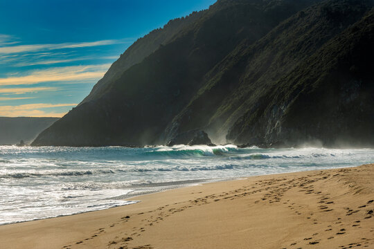 Waves crashing on the sandy shore of Quintay Beach in Chile during a bright, clear day