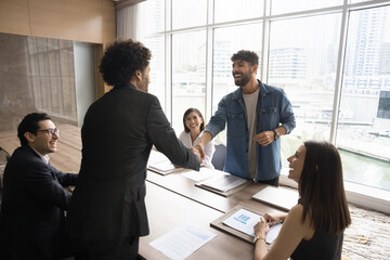 Diverse business partners shaking hands during meeting in modern office conference room, succeed...