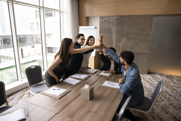 Confident happy teammates giving high five gesture, clapping hands over conference table, celebrate effective, productive teamwork accomplishment, share joint advancement, enjoy successful cooperation