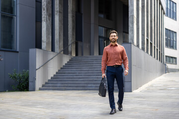A successful businessman in full growth walks through the city with a business bag in his hands, a mature man smiles contentedly from outside an office building.