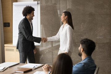 Young Asian employee get appreciated or awarded for skills and professional achievements, shake hands company boss praising her, congratulate with promotion or reward during group meeting in boardroom