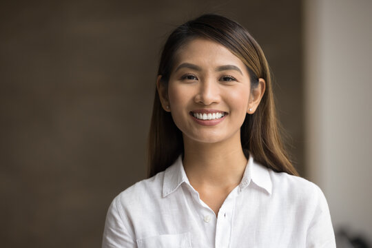 Close up head shot portrait of young smiling Asian businesswoman wear white shirt posing in office, looks positive, feels happy, gazing at camera. Professional occupation or teacher, profile picture