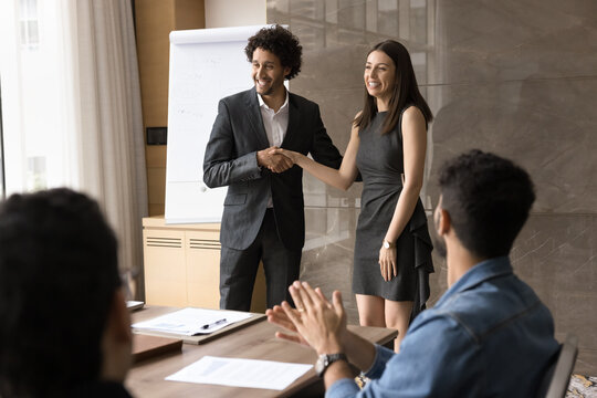 Boss presenting new female employee during group briefing in boardroom, hold her hand, encourages, congratulate with reward or promotion while staff members clapping their hands as recognition gesture