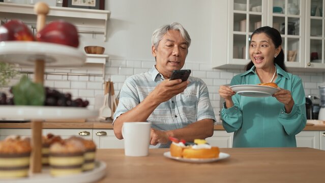 Senior manager calling his colleague about financial project while looking at wife serving breakfast. Grandmother supporting grandfather and giving him breakfast while elder man using phone. Myrmidon.