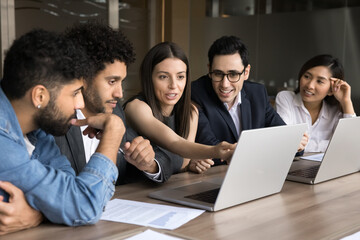 Group of young professionals, five businesspeople, focused multiethnic members working together on joint task using laptops, share ideas and strategies, developing marketing plan. Business, tech, apps