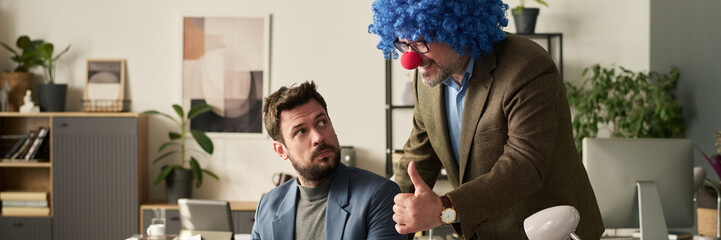 Header of happy mature male clown boss showing thumb up and looking at screen of laptop of young...