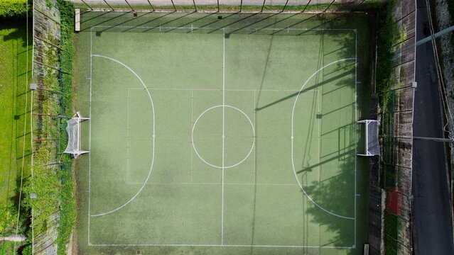 scenic aerial view from above of a green five-a-side football pitch surrounded by nets under the light of the summer sun -