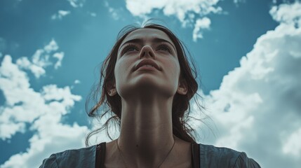 Woman with hand in hair, looking upward with contemplative expression amidst clouds in sky.